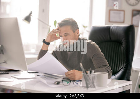 Mature serious architect with papers looking at sketches while checking them Stock Photo