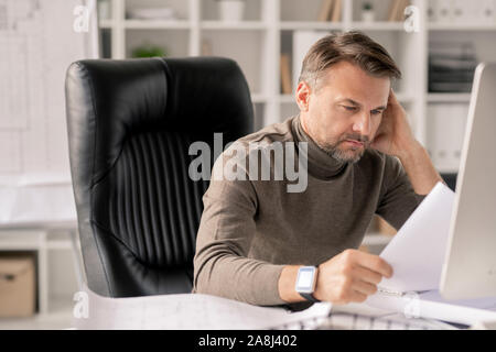Mature engineer with papers looking at one of sketches while checking them Stock Photo