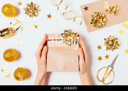 Female hands holding gift bag among golden Christmas decorations and confetti, flat lay. Stock Photo