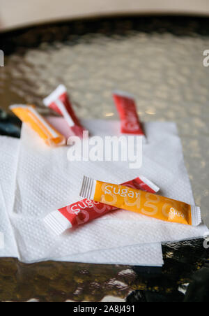 multi-colored paper bags with sugar lie on a napkin on a glass table Stock Photo