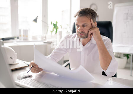 Mature pensive engineer looking at sketch while thinking of ideas or checking it Stock Photo