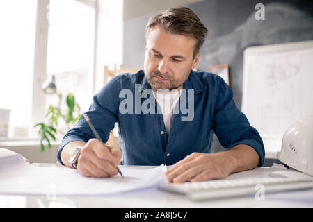 Serious architect with pencil drawing new sketch on paper while bending by desk Stock Photo