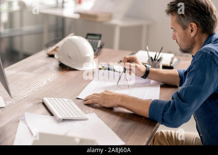Serious mature engineer in casualwear using dividers while drawing sketch Stock Photo