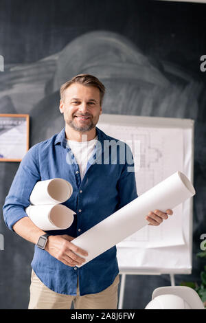Successful mature engineer with rolled blueprints standing in front of camera Stock Photo
