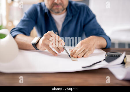 Hands of modern engineer with pencil and ruler drawing line on blueprint Stock Photo