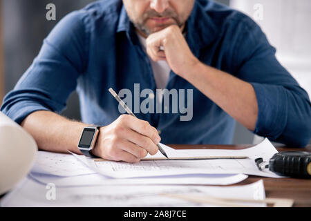 Hands of modern engineer holding pencil over ruler and sketch on blueprint Stock Photo
