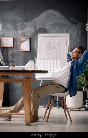 Relaxed engineer sitting on chair by table and watching video on computer screen Stock Photo