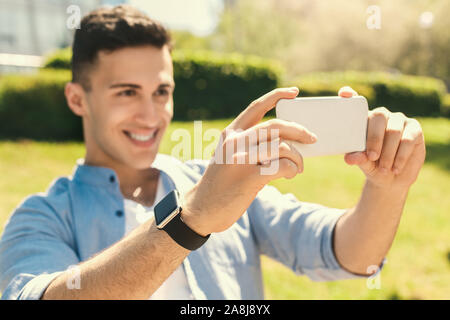Outdoors Leisure. Stylish guy wearing watch standing in park taking selfie on smartphone cheerful blurred Stock Photo