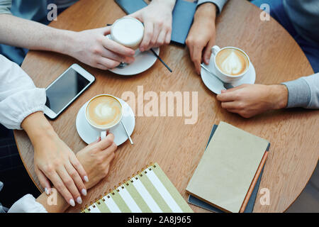 Hands of college students with gadgets and drinks gathered by table in cafe Stock Photo