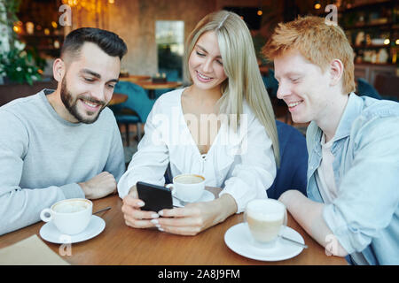 Pretty young smiling woman and two happy guys watching video in smartphone Stock Photo