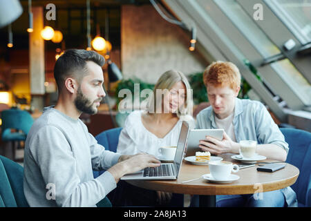 Young student with laptop networking on background of his friends using touchpad Stock Photo
