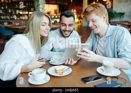 Cheerful man showing his friends curious video in tablet while relaxing in cafe Stock Photo