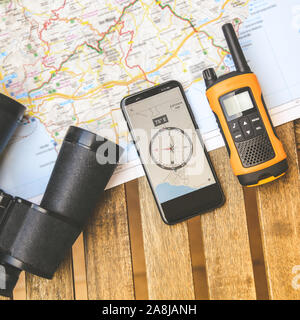 Still life view from above of adventurous objects. Walkie talkie, binoculars and electronic compass on smartphone over a map, ready for planning a new Stock Photo