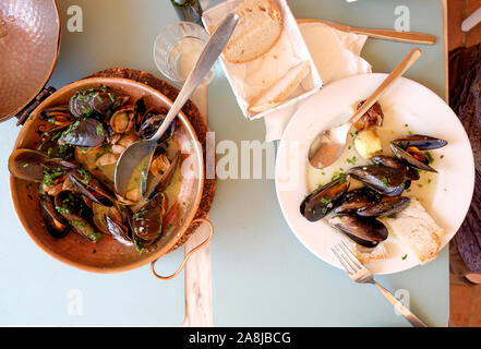 a restaurant table with a copper serving bowl and white plate full of mussels and clams, garlic and parsley a traditional Portuguese dish called Ameij Stock Photo