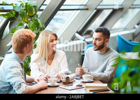 Group of students gathered by table in college cafe after classes for chat Stock Photo