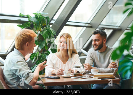 Group of young contemporary students gathered by table in cafe after classes Stock Photo