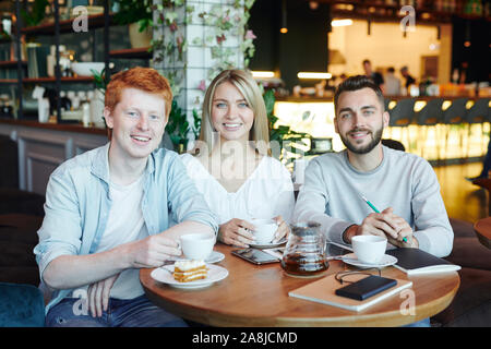 Group of cheerful students relaxing in cafe after classes and having tea Stock Photo