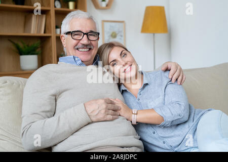 Pretty young smiling woman and her happy senior father relaxing on couch at home Stock Photo