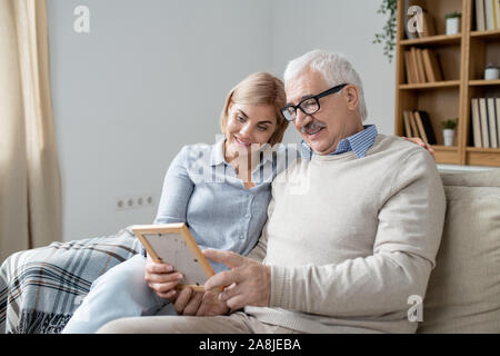 Senior man in casualwear showing his happy young daughter photo in frame Stock Photo
