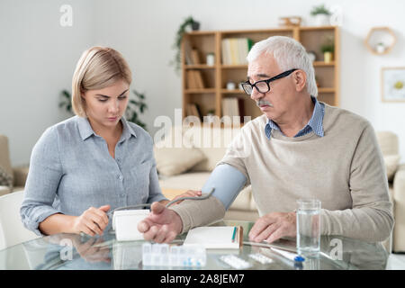 Careful daughter taking care of her sick retired father while using tonometer Stock Photo