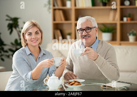 Smiling young woman and her senior father having tea by served table at home Stock Photo