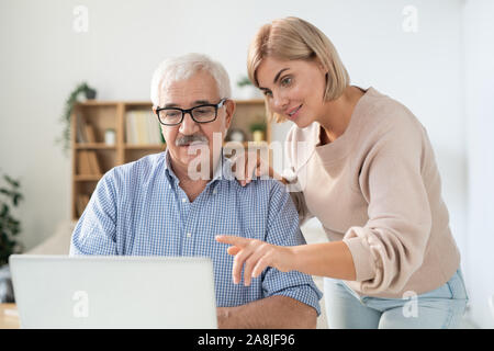 Young woman pointing at laptop display while explaining something to her father Stock Photo