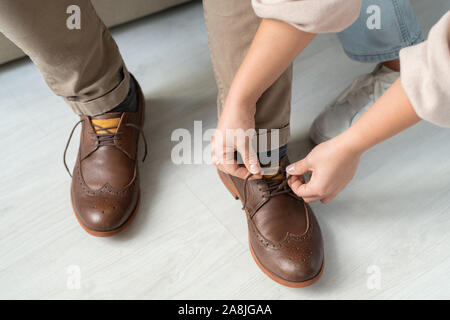 Hands of careful daughter helping senior sick father with shoelaces on boots Stock Photo