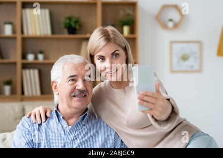 Affectionate daughter relaxing at home with her retired father and making selfie Stock Photo