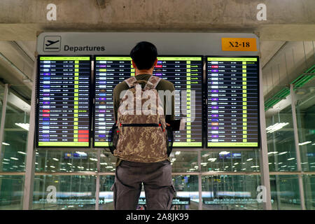 Young man with backpack looking at blurry flight information display screen at the airport Stock Photo