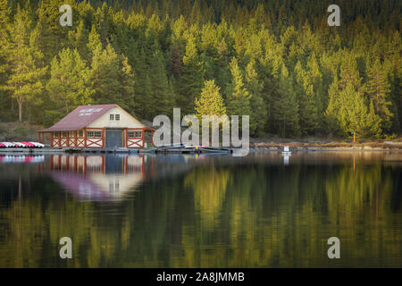 Maligne lake floating cabin. House in the border of the lake with boats, near the trees. Sunlight in the trees, reflected on the water. Jasper, Canada Stock Photo