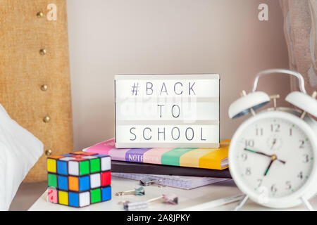 Back to school message with hashtag on lightened box with alarm clock, notebooks, magic cube and stationery on the bedside table. Good morning study m Stock Photo