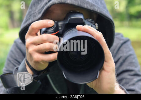 The photographer hidden with the camera. A man in a hood is taking pictures hidden. Stock Photo