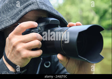 The photographer hidden with the camera. A man in a hood is taking pictures hidden. Stock Photo