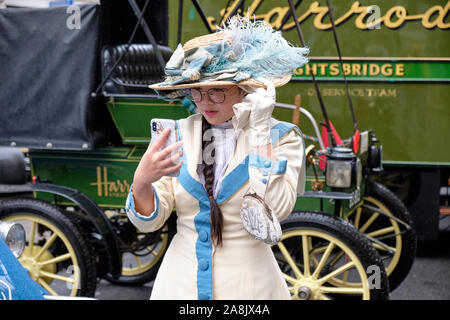Young lady in vintage Victorian clothing with feathery hat looking at her cell phone, creating anachronism Stock Photo