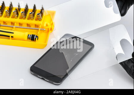 A man is holding two protective glasses for a smartphone. One is broken the other is new. Stock Photo