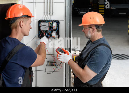 Electricians are checking the voltage at the terminals of the electrical meter. They are using a multimeter. Stock Photo