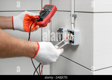 An electrician is using a multimeter to measure the voltage in a wall outlet. Stock Photo