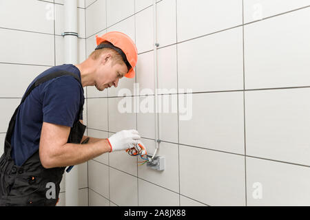 The electrician is installing an electrical outlet on the wall. Stock Photo