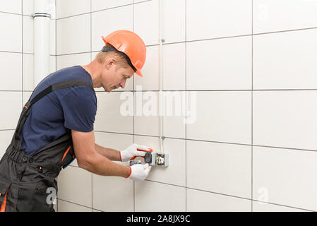The electrician is installing an electrical outlet on the wall. Stock Photo