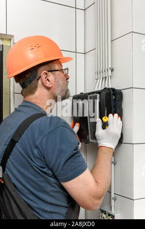 The electrician is installing an electrical meter on the wall. Stock Photo