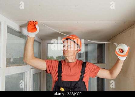 The worker is attaching the mesh to the seams between the plasterboards. Stock Photo