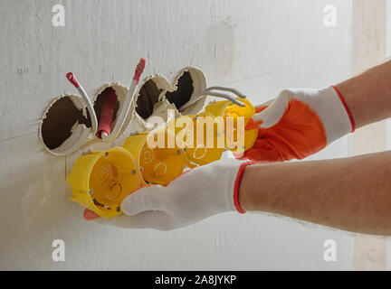 The worker is installing a group of socket boxes into drywall. Stock Photo