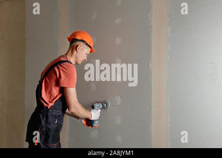 The worker is making holes in the drywall to install the outlet in the future. Stock Photo
