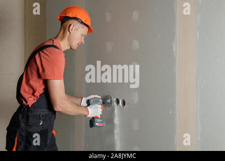 The worker is making holes in the drywall to install the outlet in the future. Stock Photo