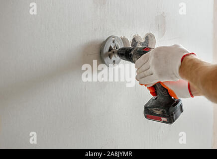 A worker is making holes in the drywall to install the outlet in the future. Stock Photo