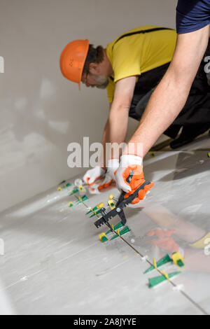 Workers are using plastic clamps and wedges to leveling the large ceramic tile on the floor. Stock Photo