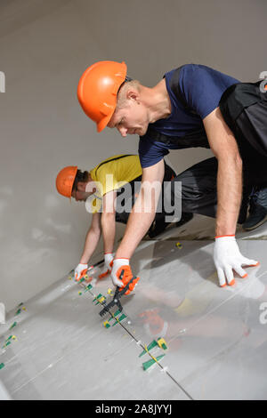 Workers are using plastic clamps and wedges to leveling the large ceramic tile on the floor. Stock Photo