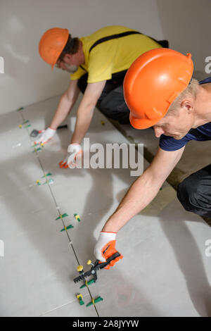 Workers are using plastic clamps and wedges to leveling the large ceramic tile on the floor. Stock Photo