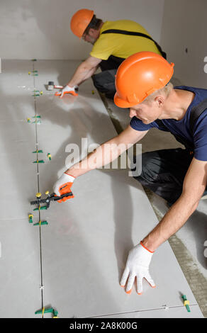 Workers are using plastic clamps and wedges to leveling the large ceramic tile on the floor. Stock Photo
