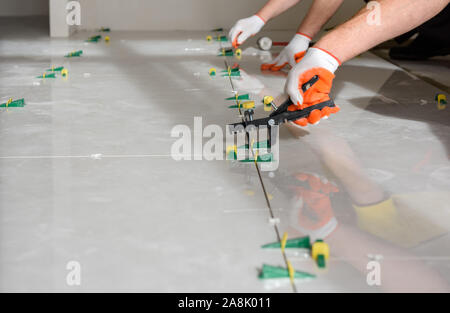 Workers are using plastic clamps and wedges to leveling the large ceramic tile on the floor. Stock Photo